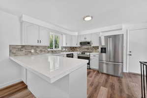 Kitchen featuring white cabinetry, light-toned quartz countertops, a tiled backsplash, stainless steel appliances, and wood-finish flooring