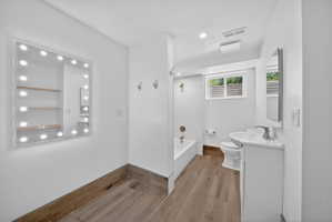 Downstairs Bathroom featuring wood-finish flooring, a contemporary vanity with a white countertop, a built-in bathtub with white subway tile surround, recessed lighting, and a large illuminated wall mirror