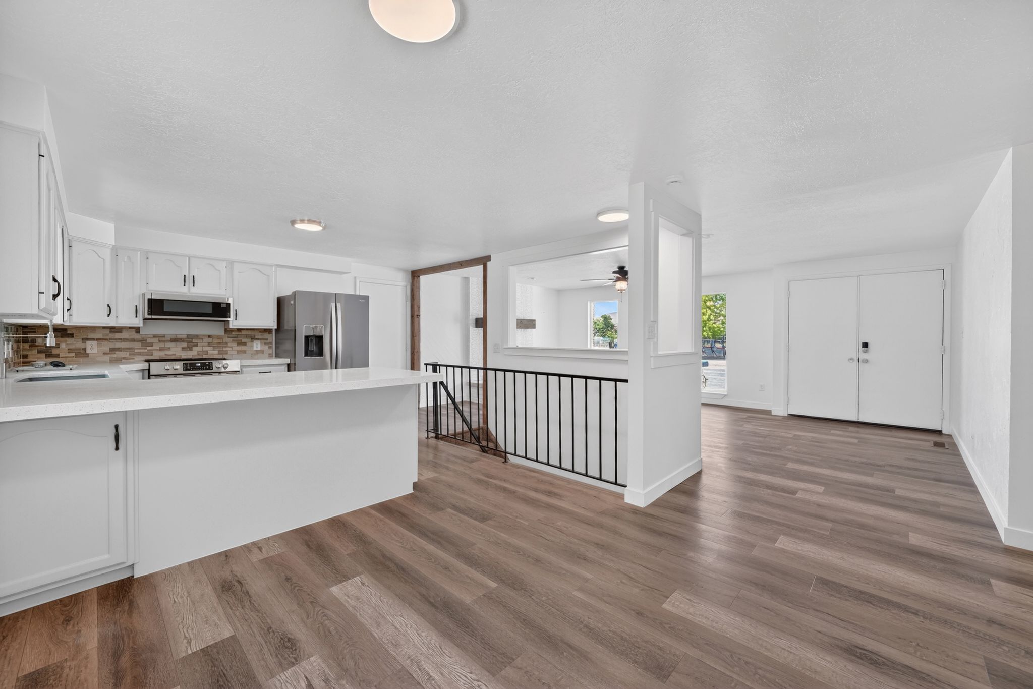 Open-concept kitchen featuring white cabinetry, stainless steel appliances, a breakfast bar, and wood-finish flooring throughout