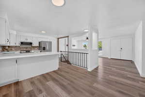 Open-concept kitchen featuring white cabinetry, stainless steel appliances, a breakfast bar, and wood-finish flooring throughout