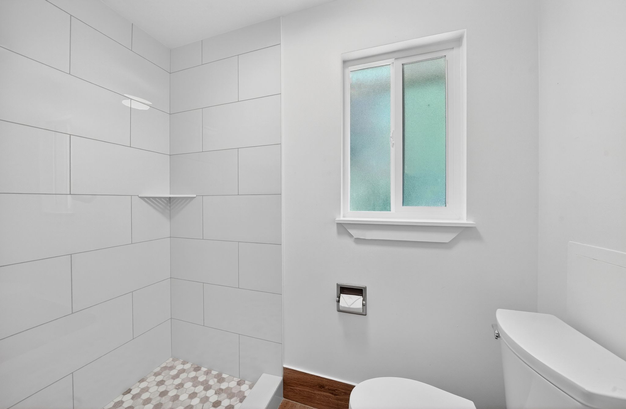 Primary Bathroom Shower with white subway tile surround, hexagon tile flooring, and integrated corner shelf