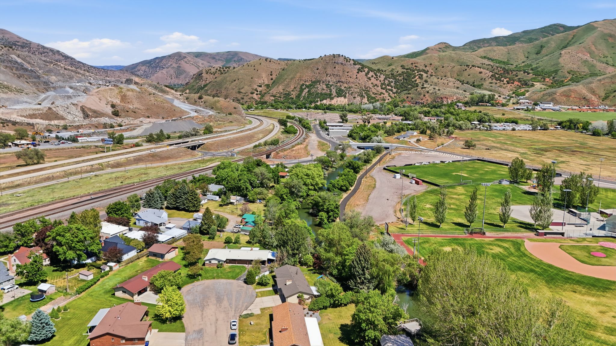 Elevated aerial perspective showcasing a neighborhood with diverse residential structures, abundant mature trees, a meandering waterway, and expansive green spaces
