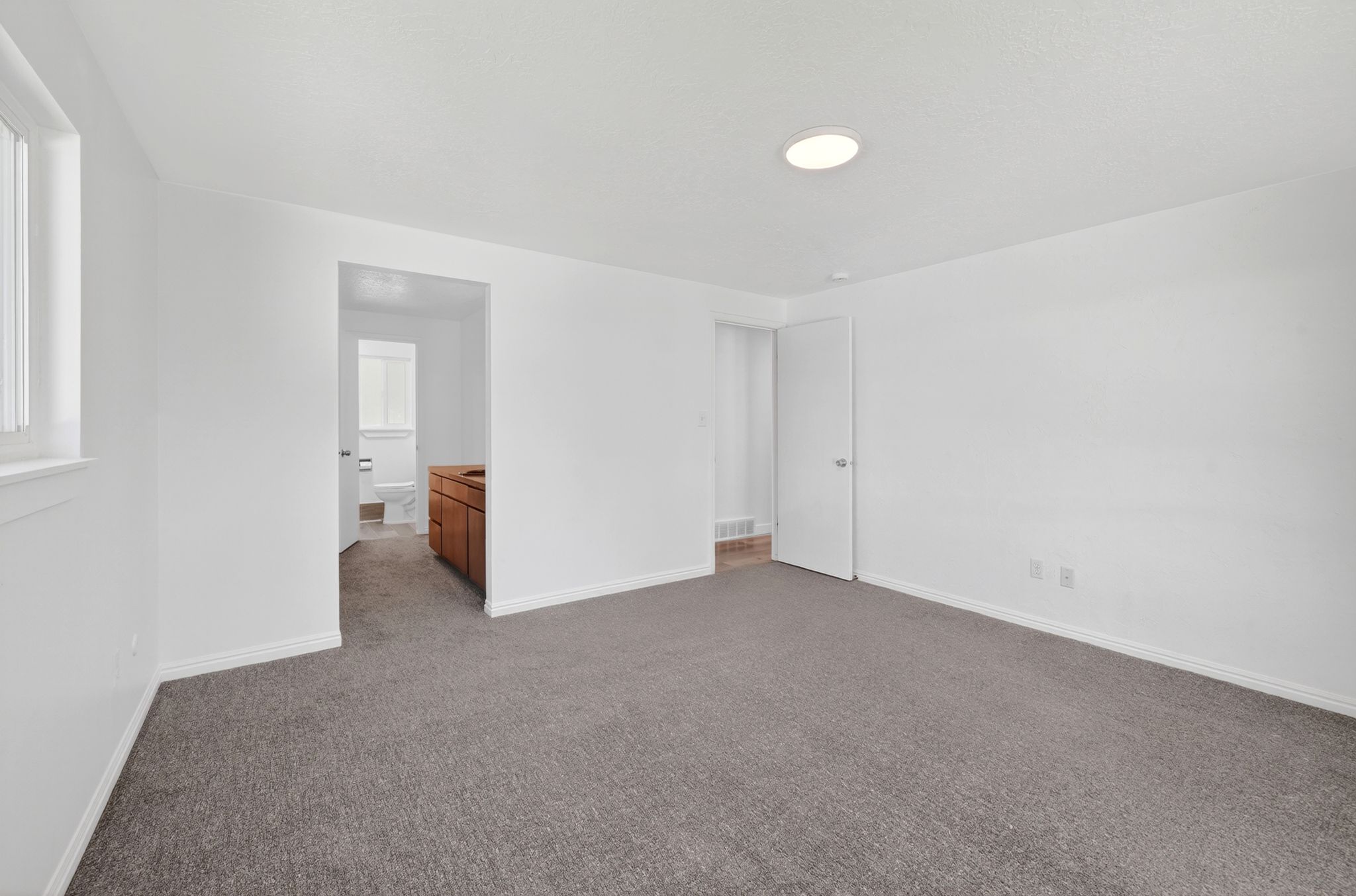 Spacious room with new gray carpet, white walls, and a large window