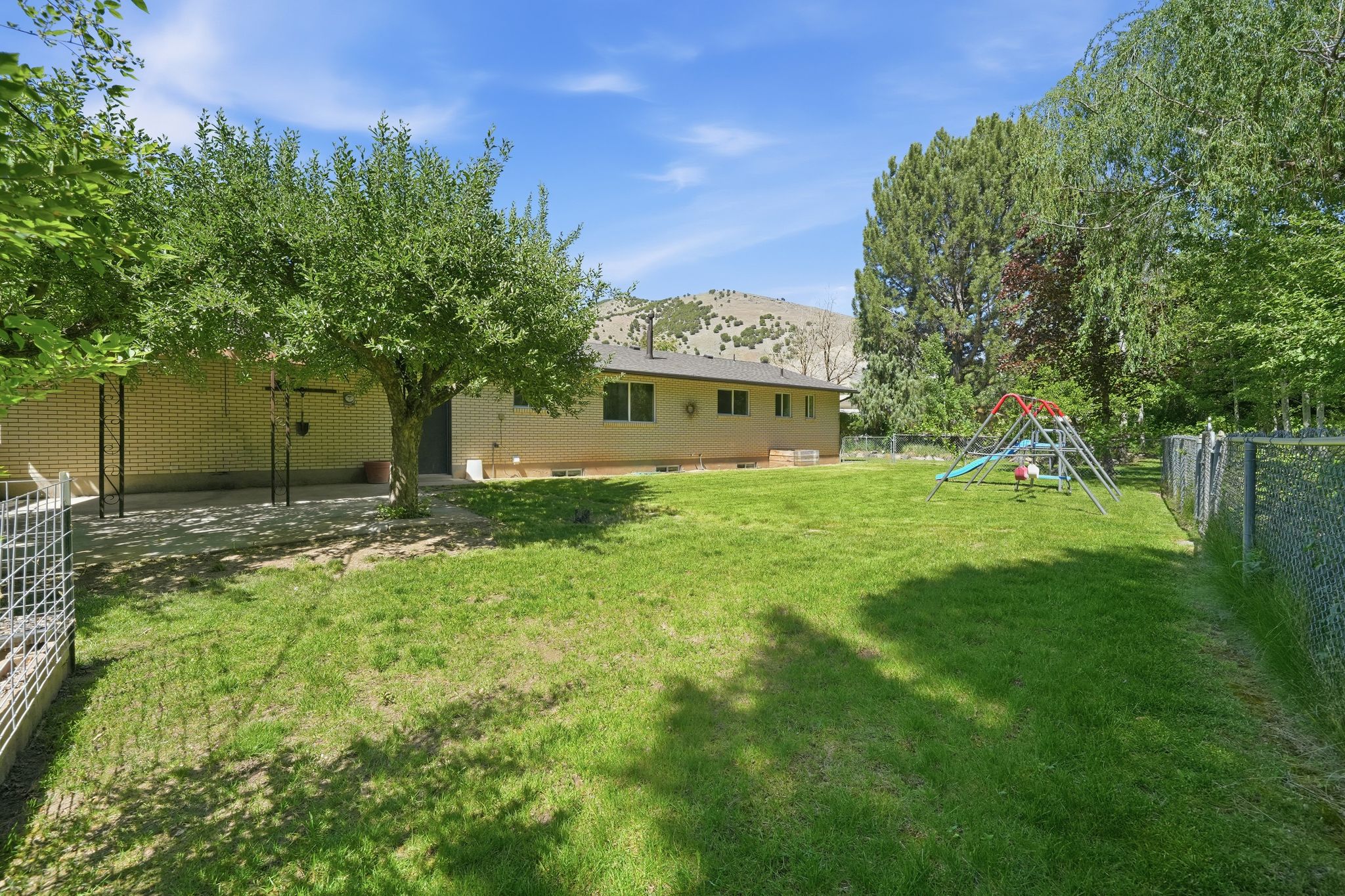Expansive rear yard featuring a large grass area, mature trees, a covered patio, and chain-link fencing