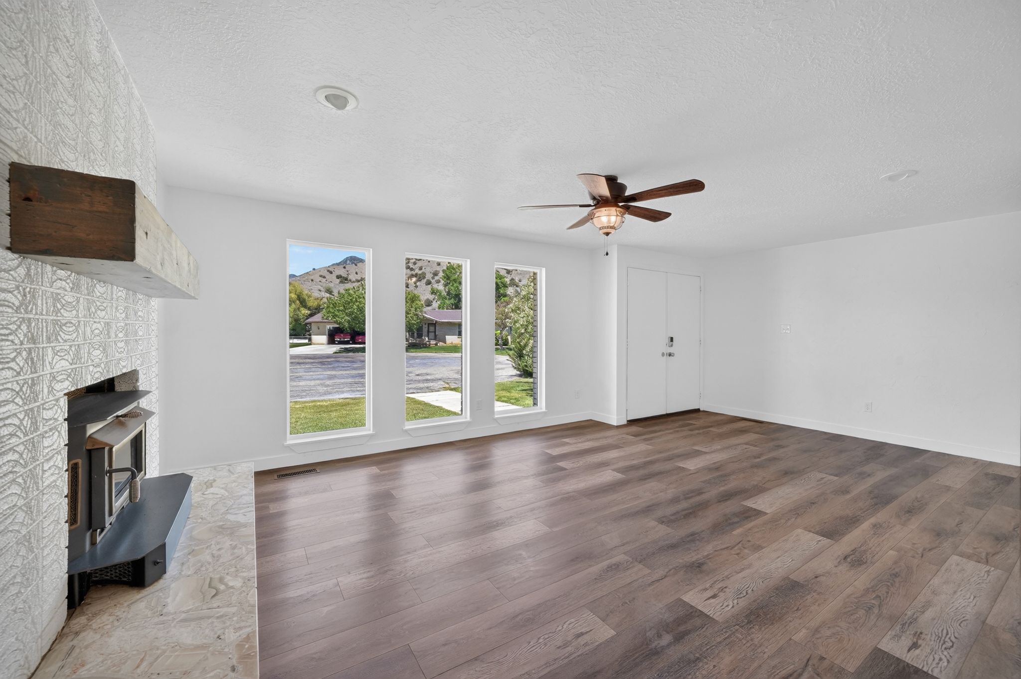 Spacious room featuring a fireplace with a wood mantle, wood-finish flooring, a ceiling fan, and multiple windows