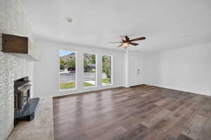 Spacious room featuring a fireplace with a wood mantle, wood-finish flooring, a ceiling fan, and multiple windows