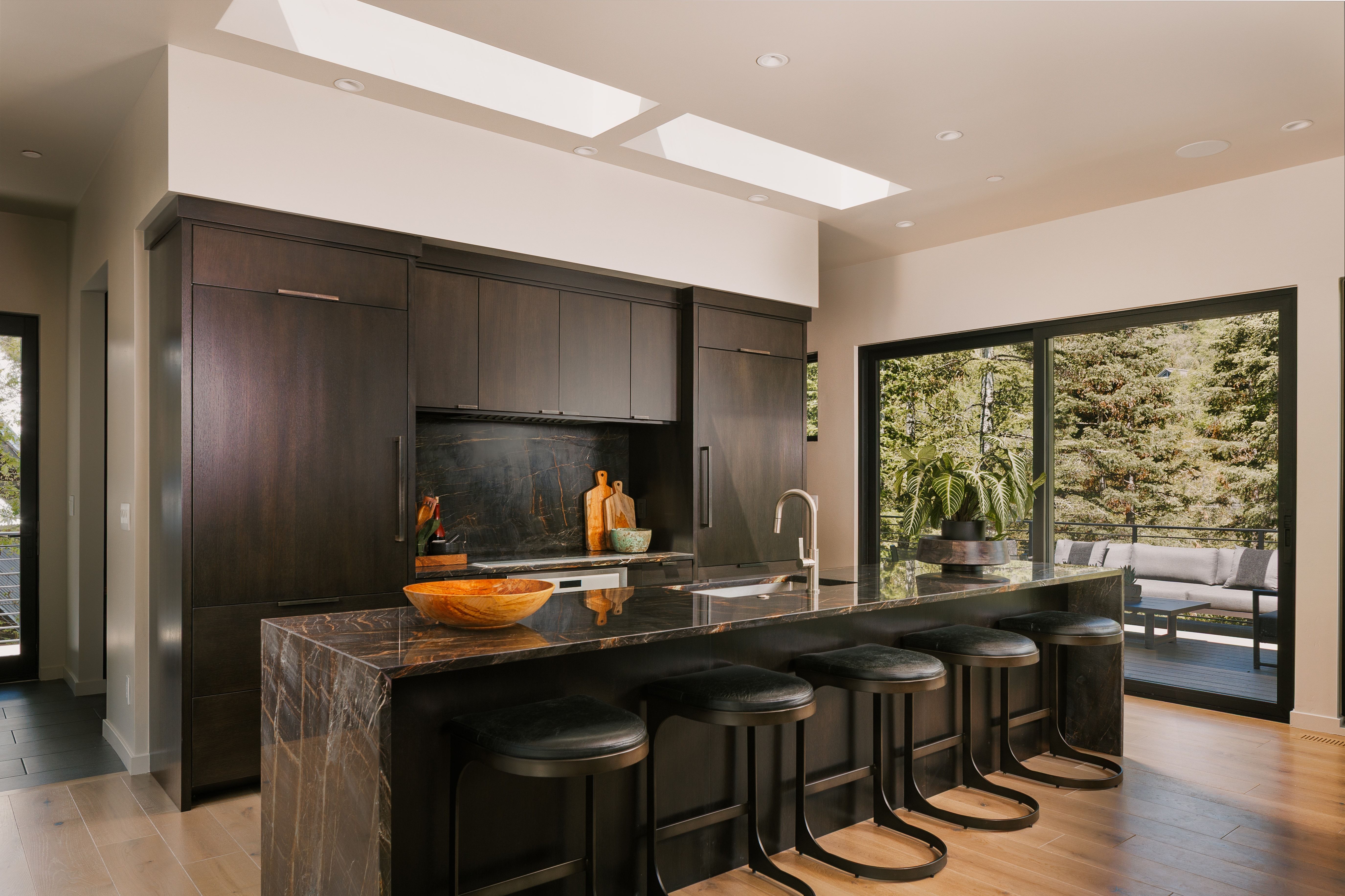 Modern kitchen with dark wood-finish cabinetry, an expansive island with a waterfall countertop, and integrated appliances
