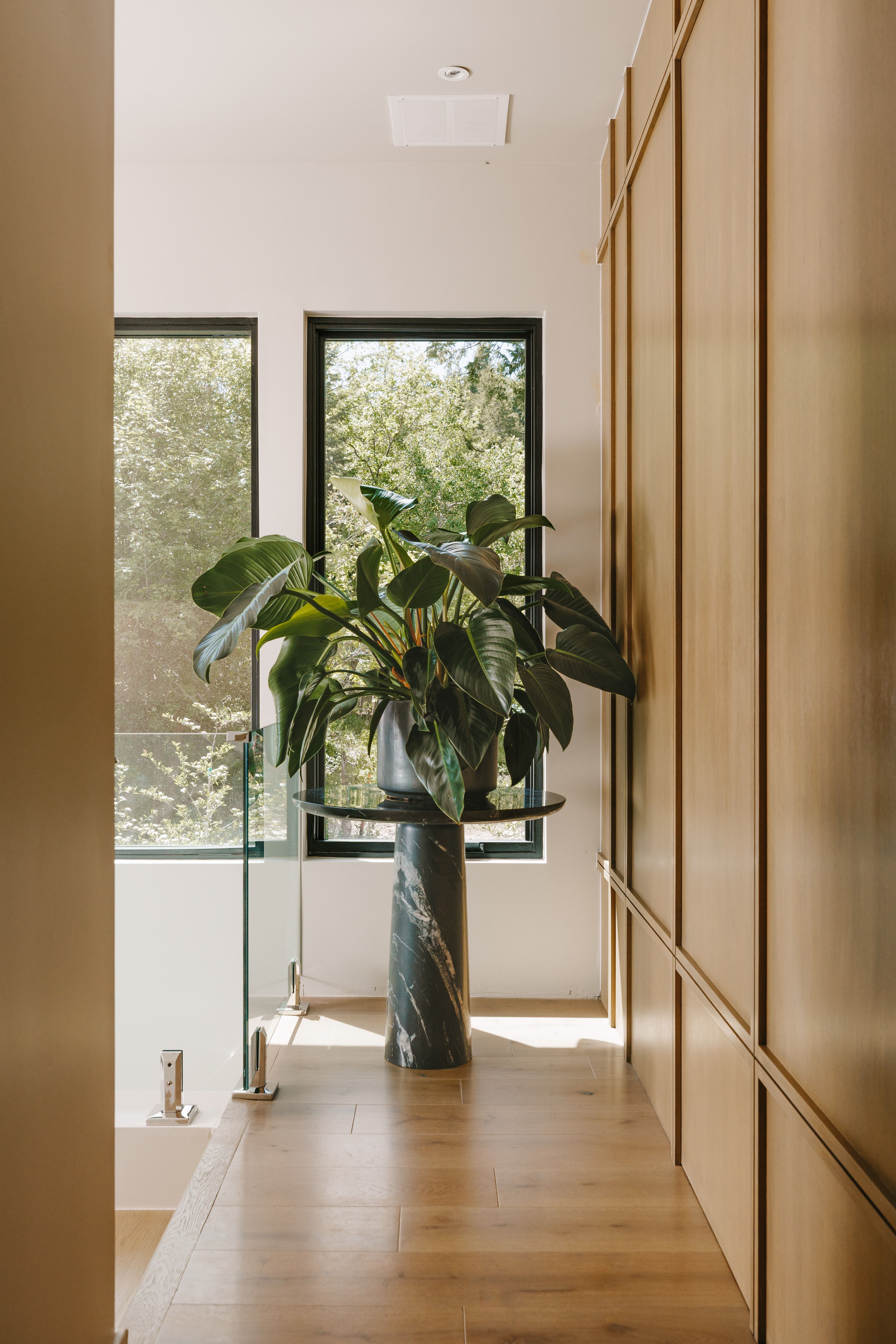 Hallway with wood-finish flooring, full-height paneled walls, and a glass railing system