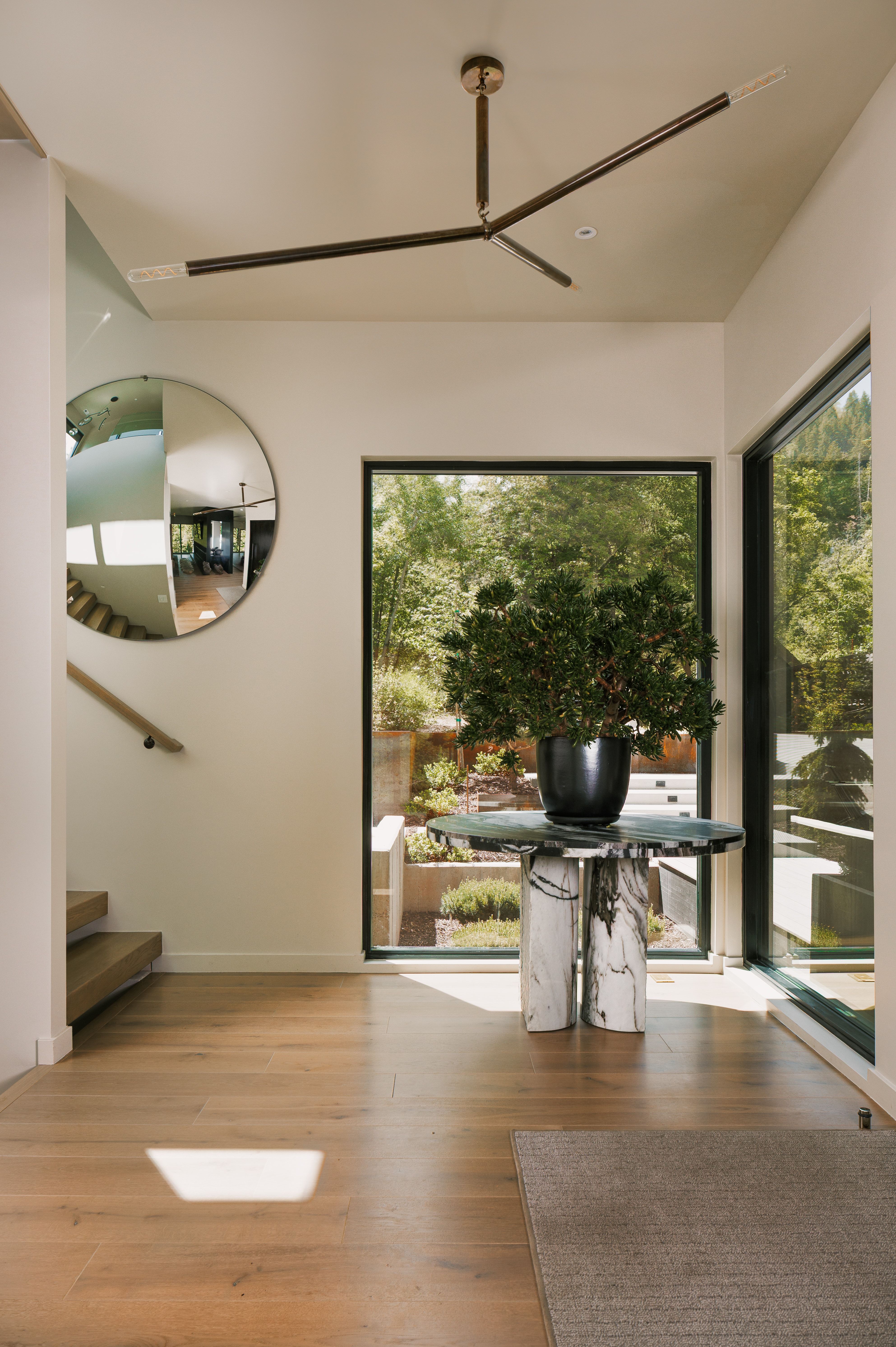 Entryway featuring wood-finish flooring, a contemporary chandelier, and a prominent floor-to-ceiling window showcasing exterior landscaping