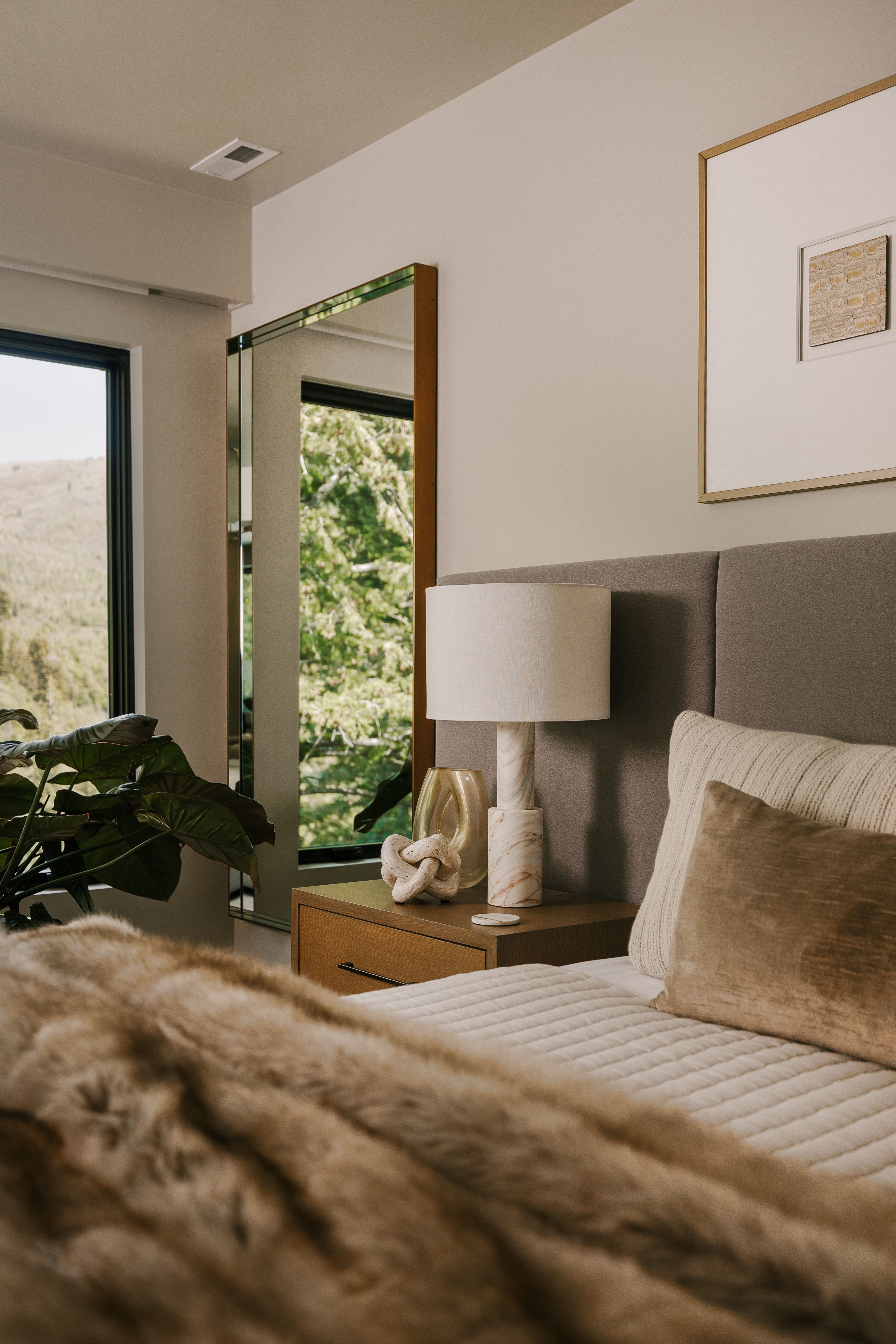 Bedroom featuring an upholstered headboard, a wood-finish nightstand, a built-in mirror, and expansive windows