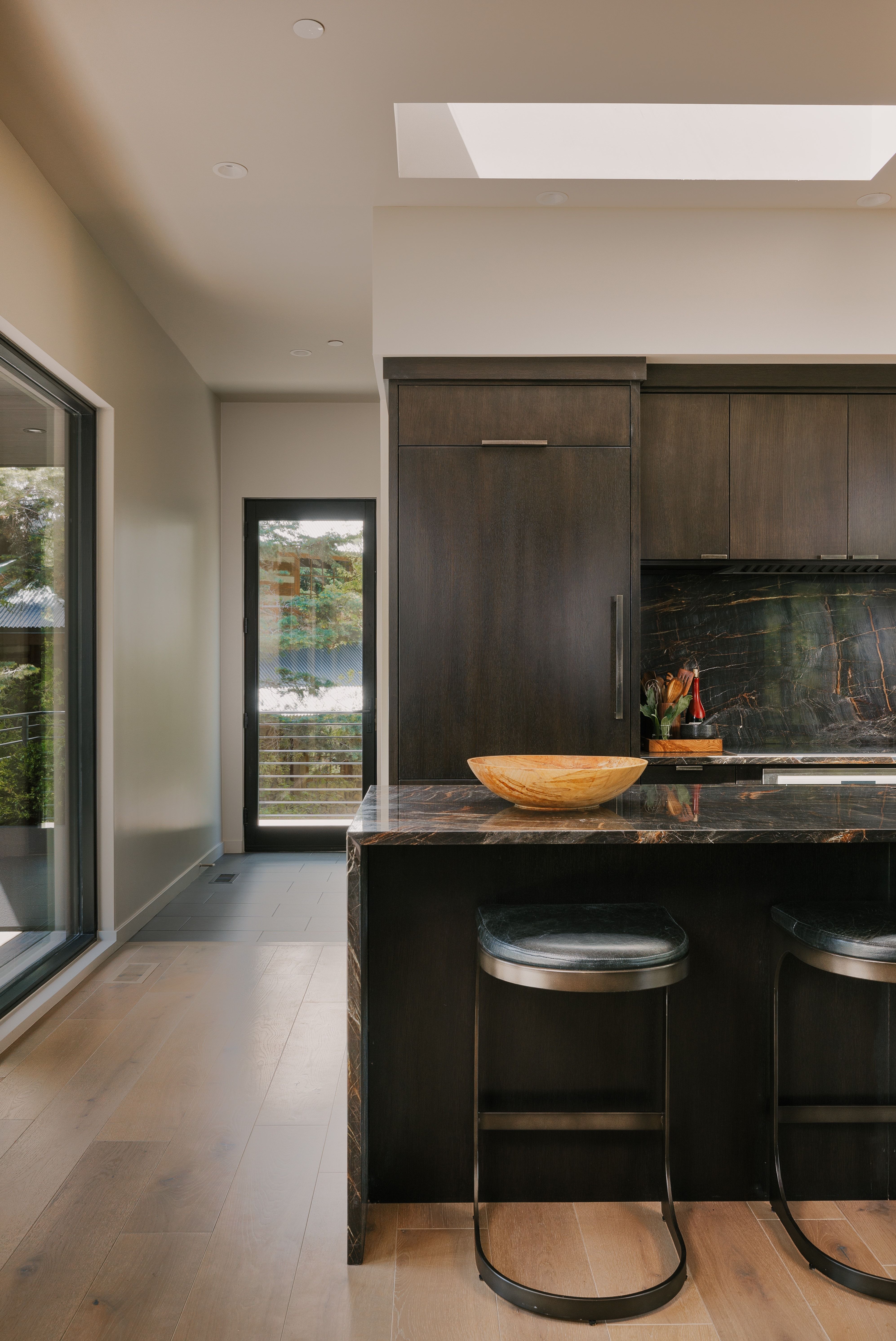 Modern kitchen island featuring a waterfall countertop, dark wood-finish cabinetry, and a black stone-finish backsplash