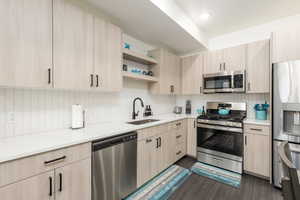 Modern kitchen featuring light wood-finish cabinetry, white countertops, and a full suite of stainless steel appliances including a refrigerator, range, microwave, and dishwasher