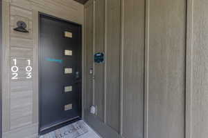 Modern exterior entry featuring a dark-finish door with multiple rectangular glass insets, a black wall-mounted sconce, and textured vertical siding