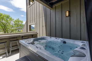 Outdoor hot tub situated on a concrete patio, featuring a built-in bar with seating, wood-paneled exterior walls, and a wall-mounted light fixture