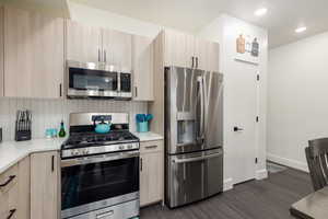 Modern kitchen featuring stainless steel appliances, light wood-finish cabinetry, a white subway tile backsplash, and dark wood-finish flooring