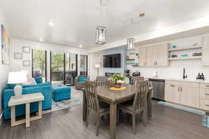 Open-concept living area featuring wood-finish flooring, a contemporary kitchen with light wood-finish cabinetry, stainless steel appliances, and a tiled backsplash