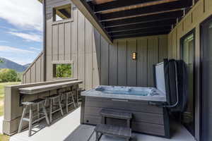 Outdoor patio featuring a built-in bar with seating, an integrated hot tub, and a wall-mounted exterior light fixture
