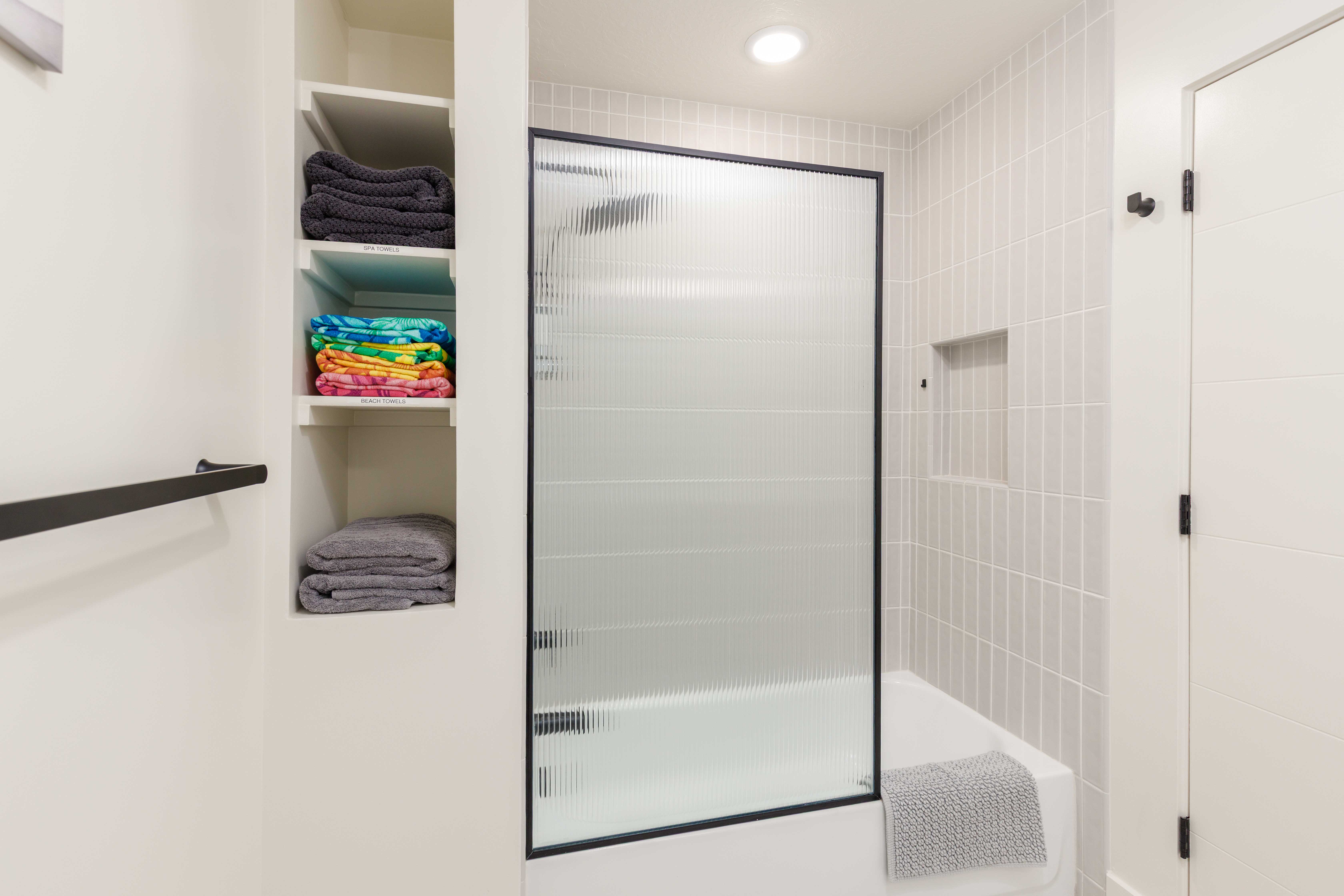 Bathroom featuring a tub/shower combination with a fluted glass and black-framed shower door, light-toned vertical tile surround, and a recessed shower niche