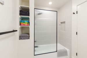 Bathroom featuring a tub/shower combination with a fluted glass and black-framed shower door, light-toned vertical tile surround, and a recessed shower niche