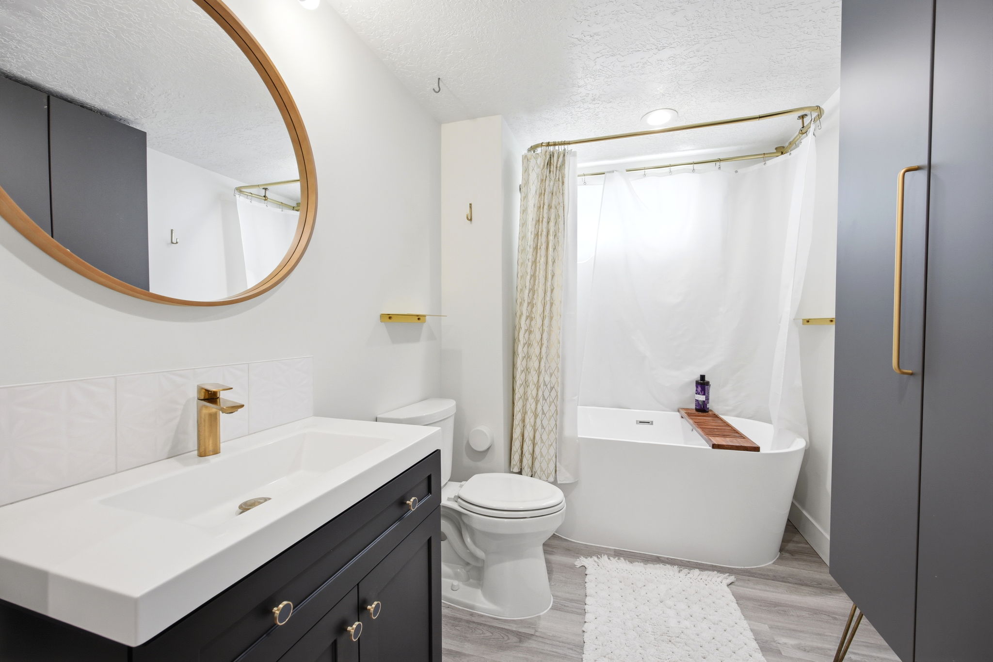 Contemporary bathroom featuring a freestanding tub, a sleek vanity with a gold-tone faucet, a large oval mirror, and a built-in shower with a curved gold-tone rod