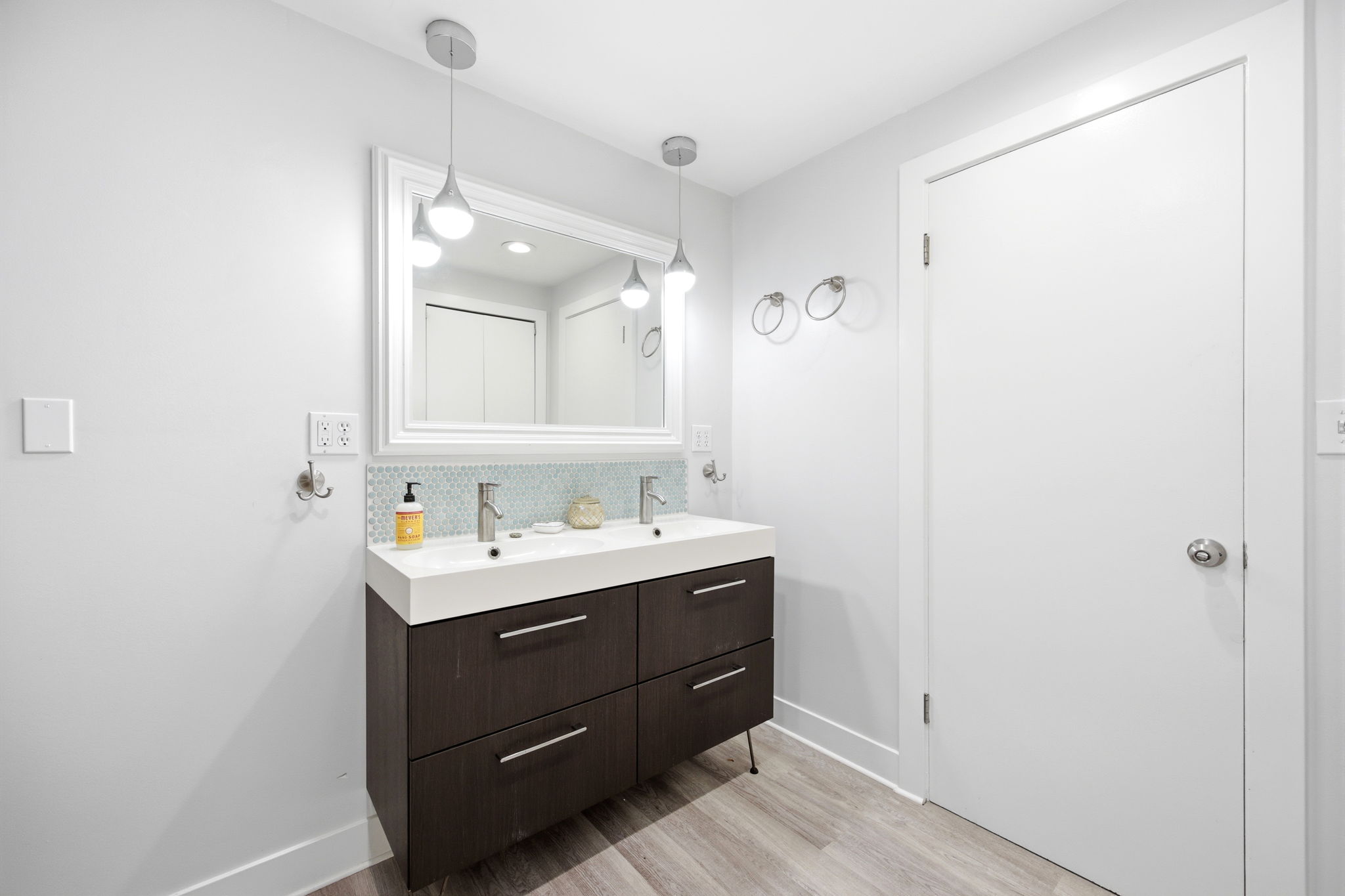 Double vanity with integrated sinks, modern dark wood-finish cabinetry, and a light blue mosaic tile backsplash