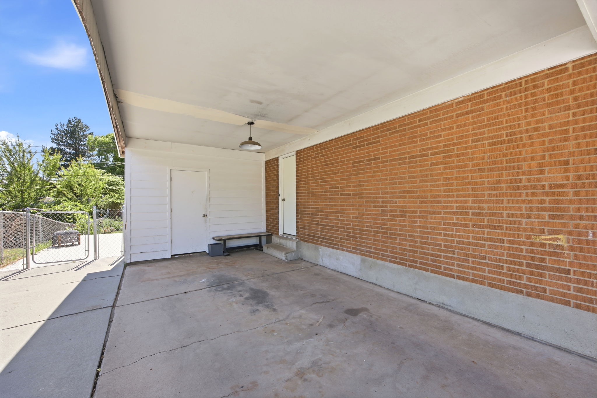 Carport with concrete slab flooring, brick exterior wall, and white siding