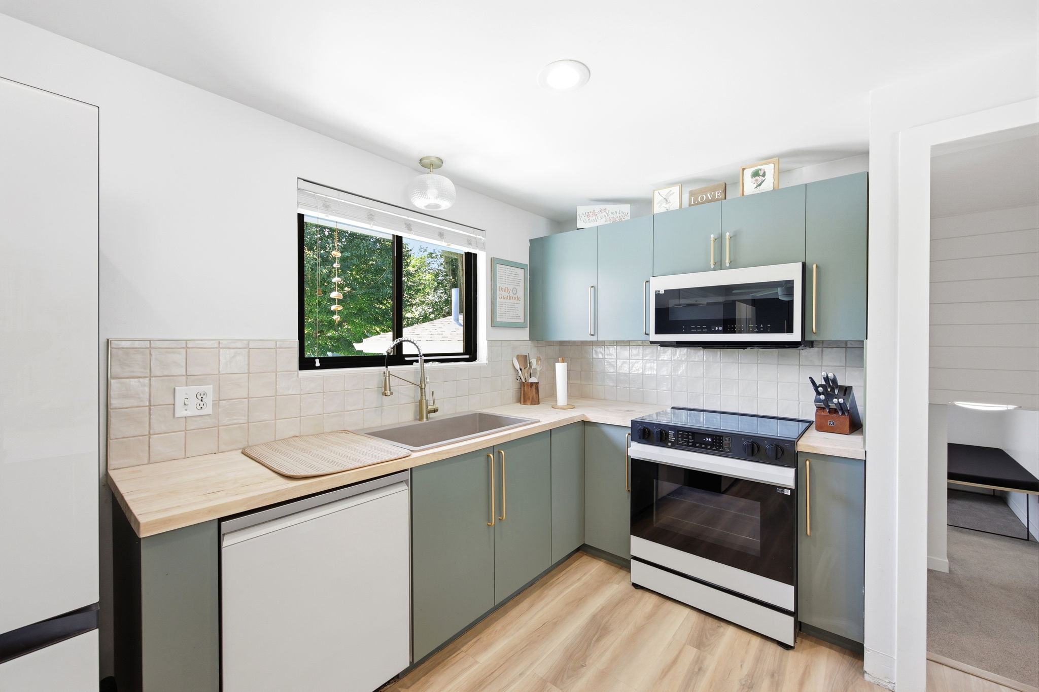 Modern kitchen featuring light green cabinetry, wood-finish countertops, stainless steel sink, and light-toned tile backsplash