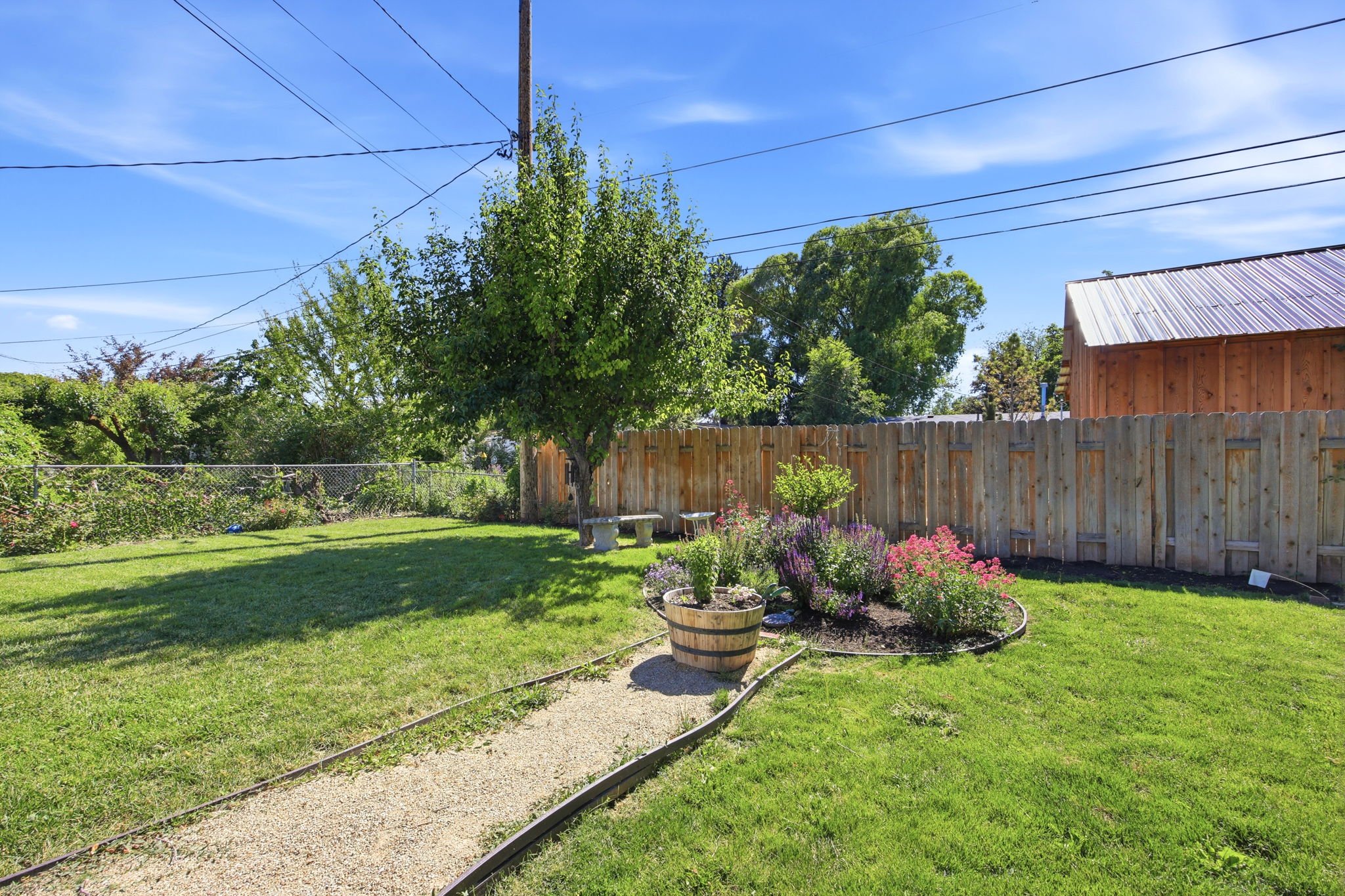 Spacious backyard featuring a lush lawn, mature trees, a gravel pathway, and a wood privacy fence
