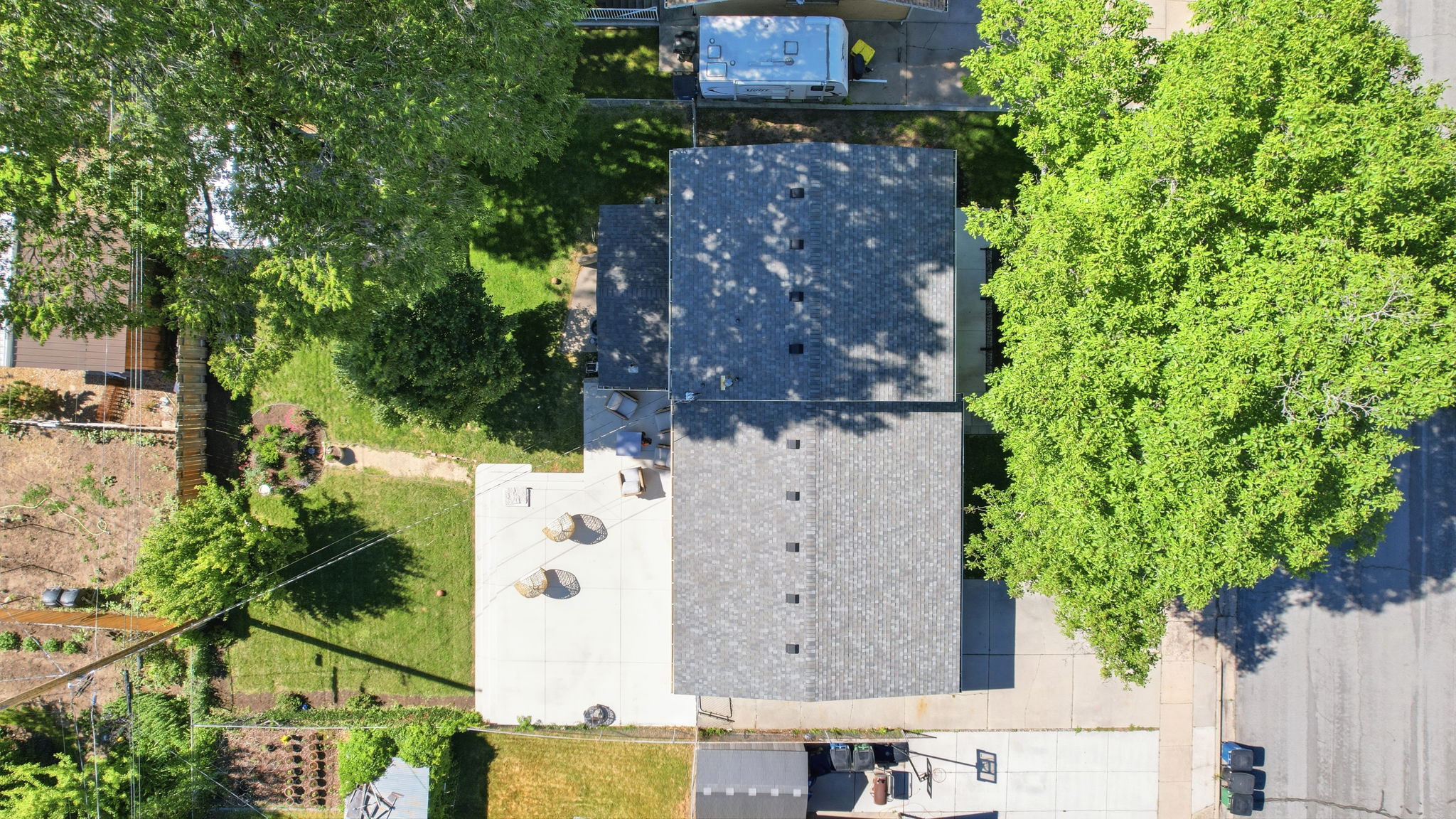 Overhead property view featuring a residence with a shingled roof, a paved patio, and a grass lawn