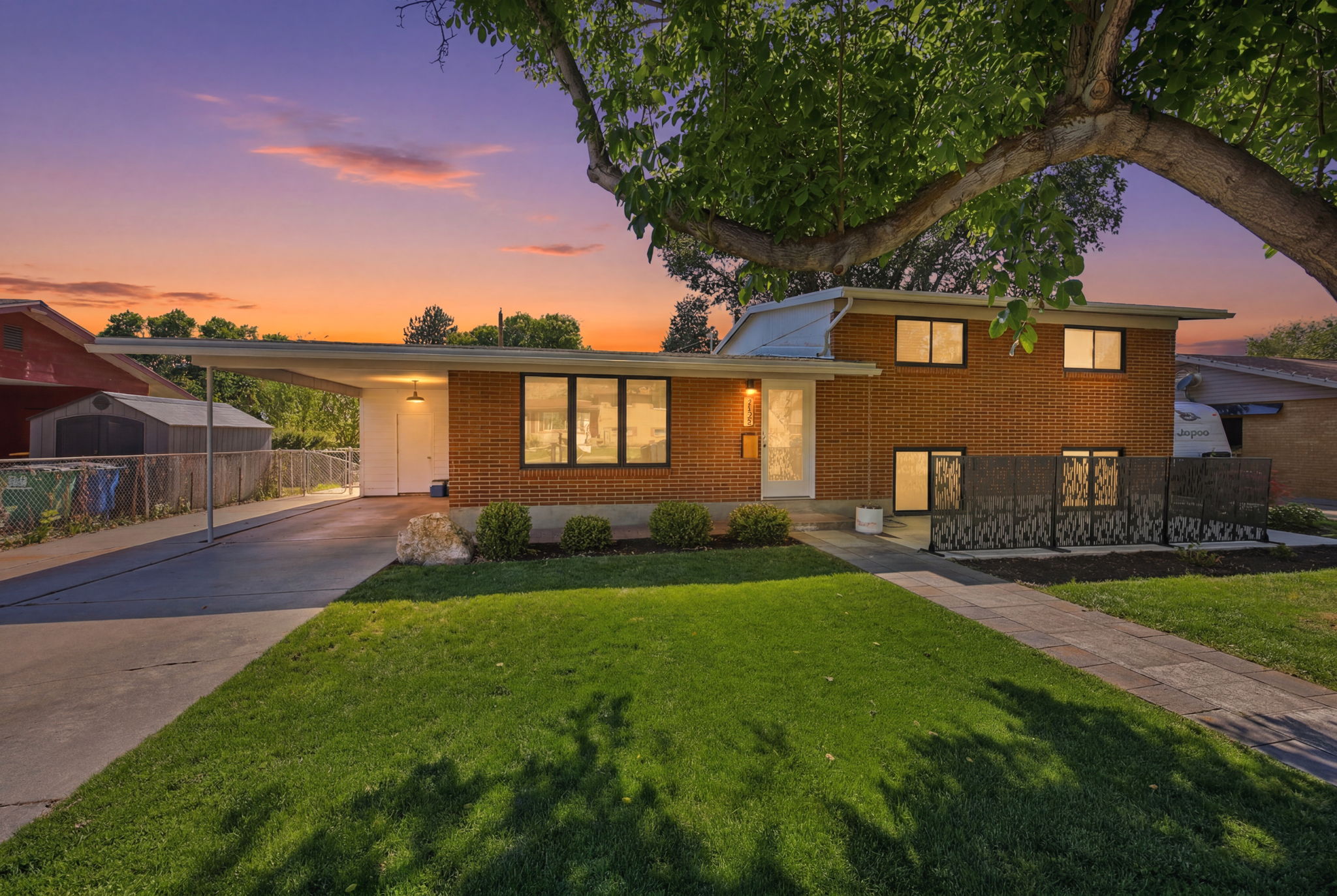 Brick facade residence featuring a covered carport, mature front yard tree, manicured lawn, and decorative privacy screens