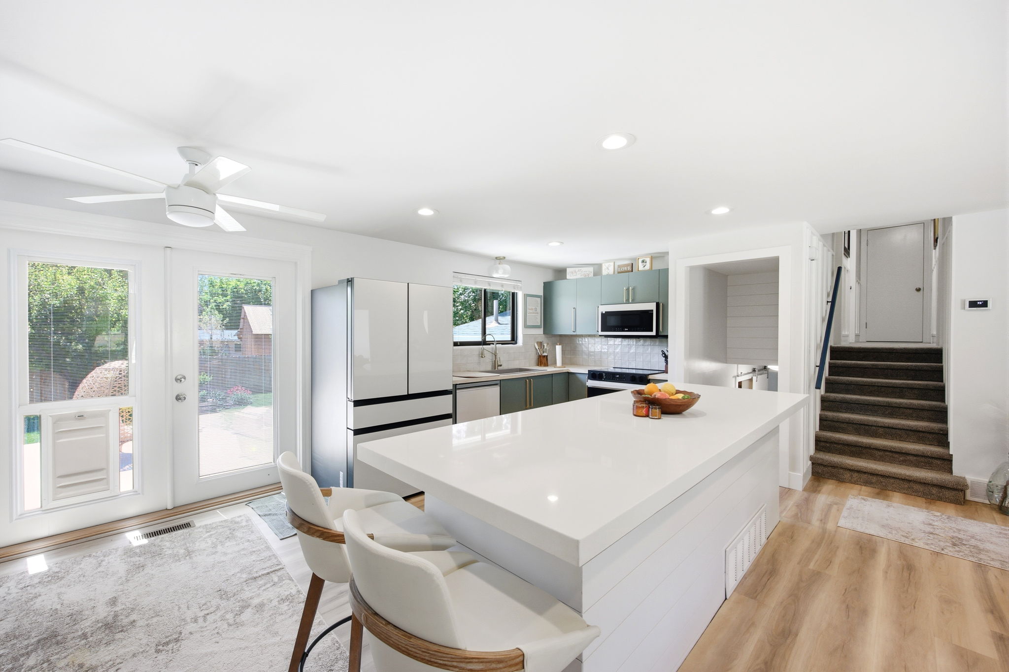 Bright kitchen featuring a large central island with a solid surface countertop, recessed lighting, wood-finish flooring, and shaker-style cabinetry with a subway tile backsplash