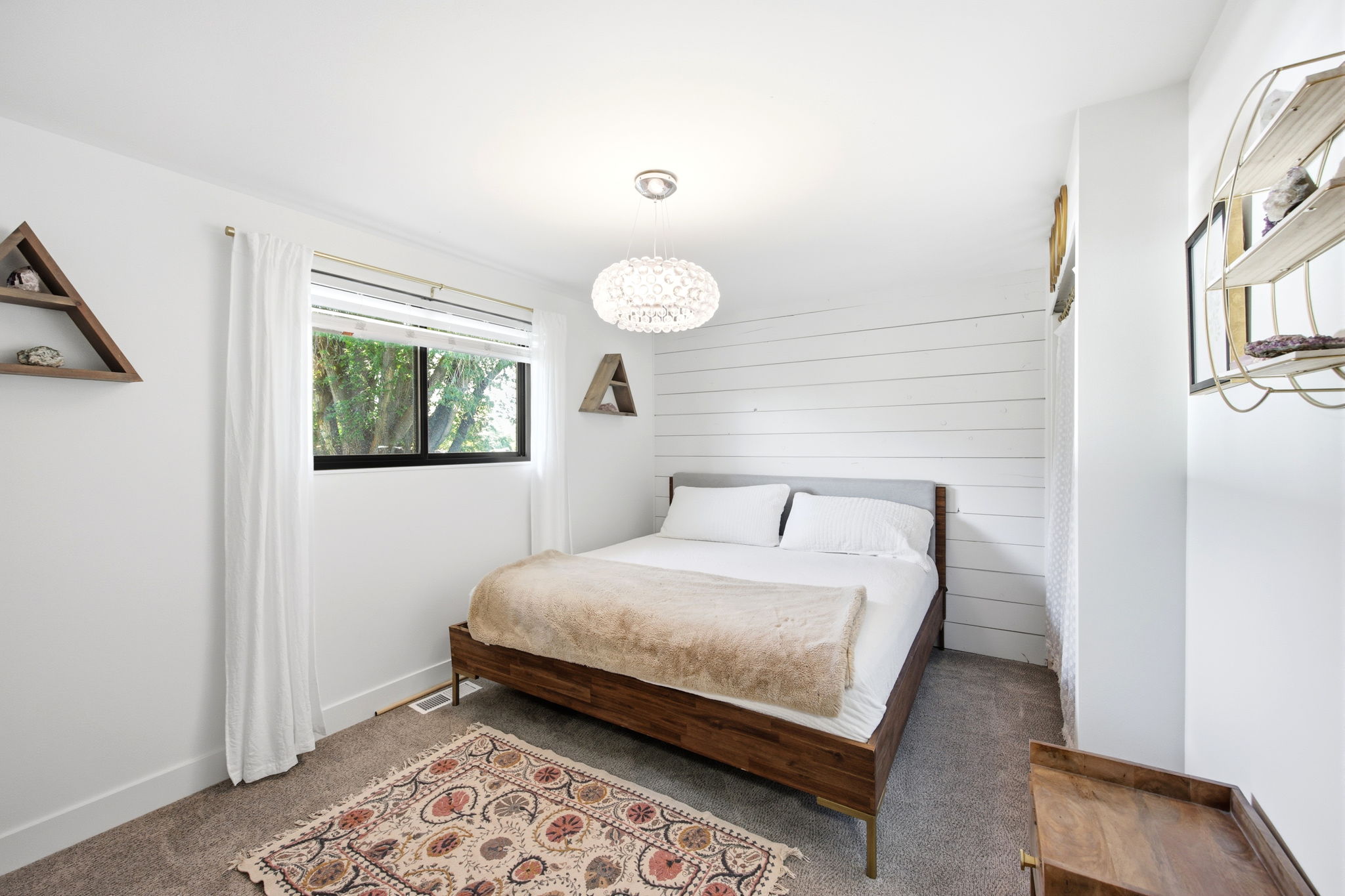 Carpeted bedroom featuring a shiplap accent wall, white walls, and a window with a dark frame