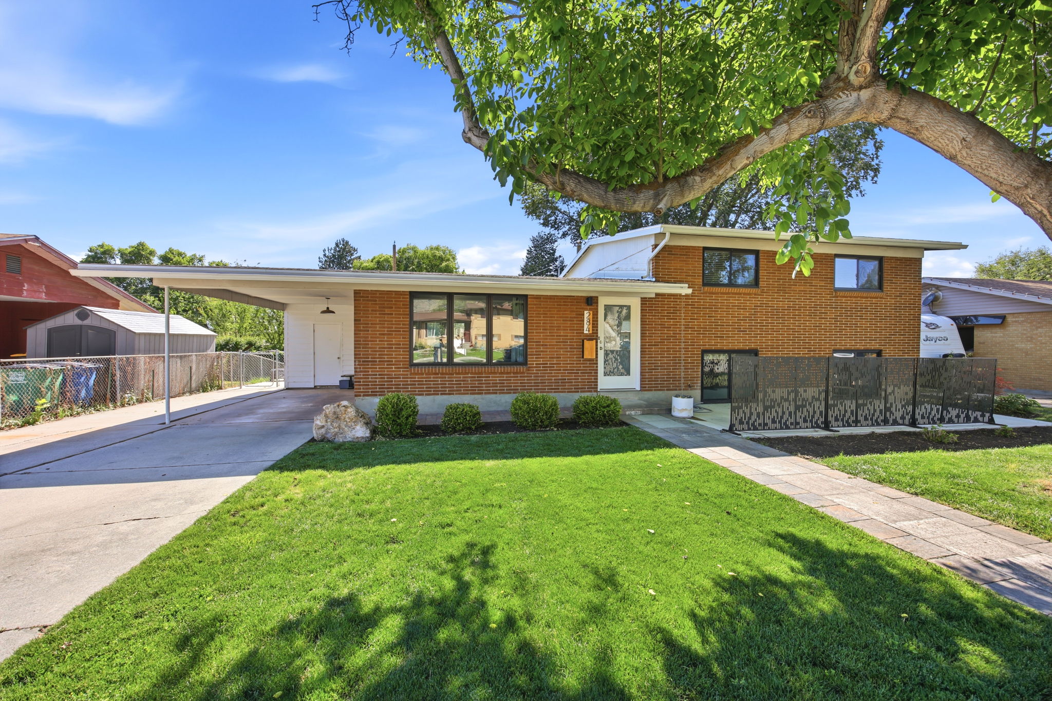 Mid-century brick exterior featuring a covered carport, manicured lawn, concrete driveway, and front walkway