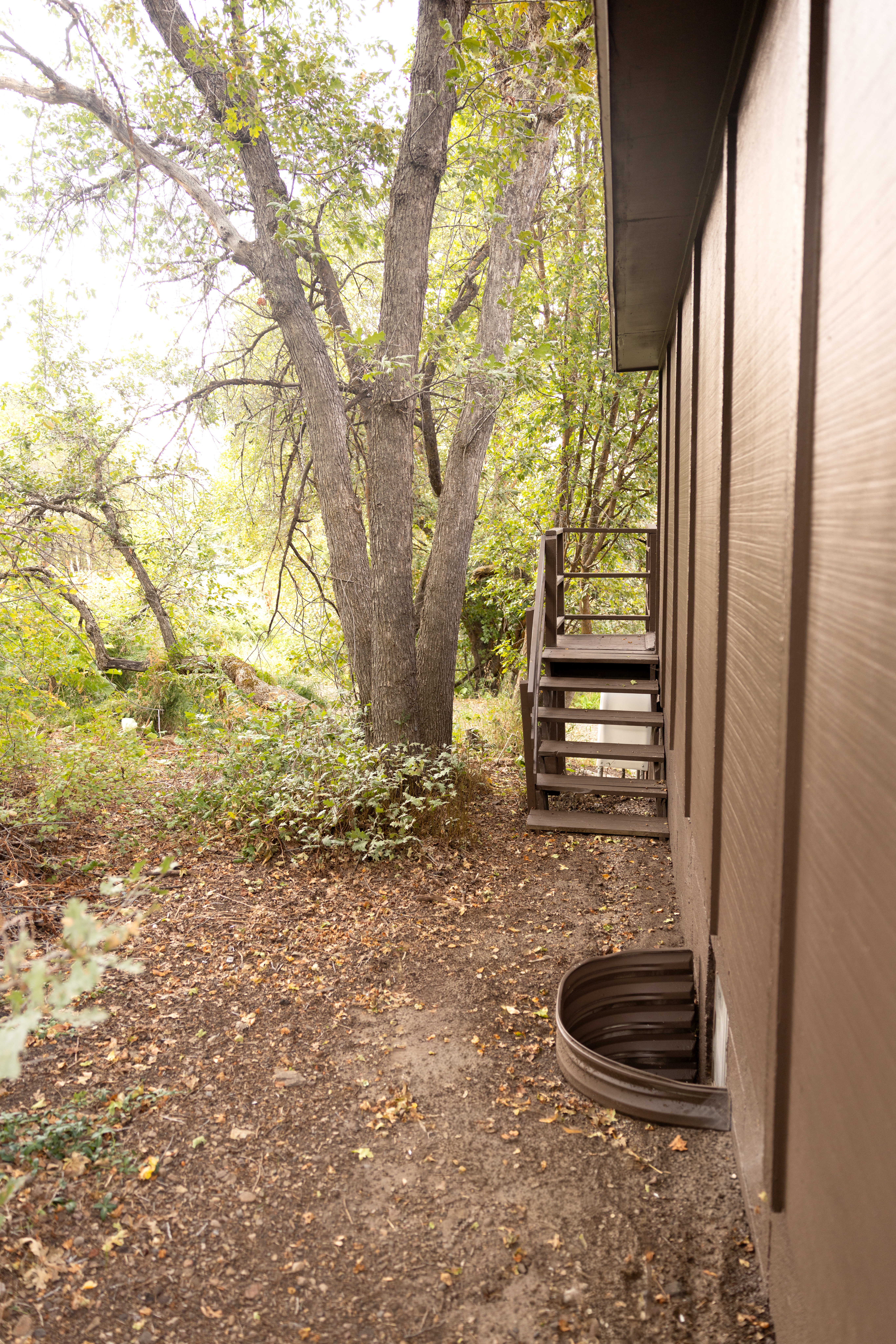 Side exterior with brown vertical siding, a window well, and wooden stairs with railings