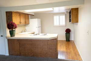 Kitchen area featuring a peninsula with countertop, wood-finish cabinetry, a white refrigerator, and a window with plantation shutters