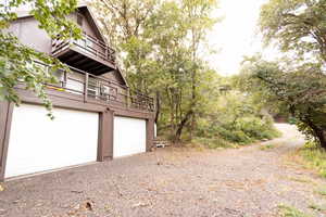 A-frame exterior with two balconies, dual garage doors, and a gravel driveway surrounded by mature trees