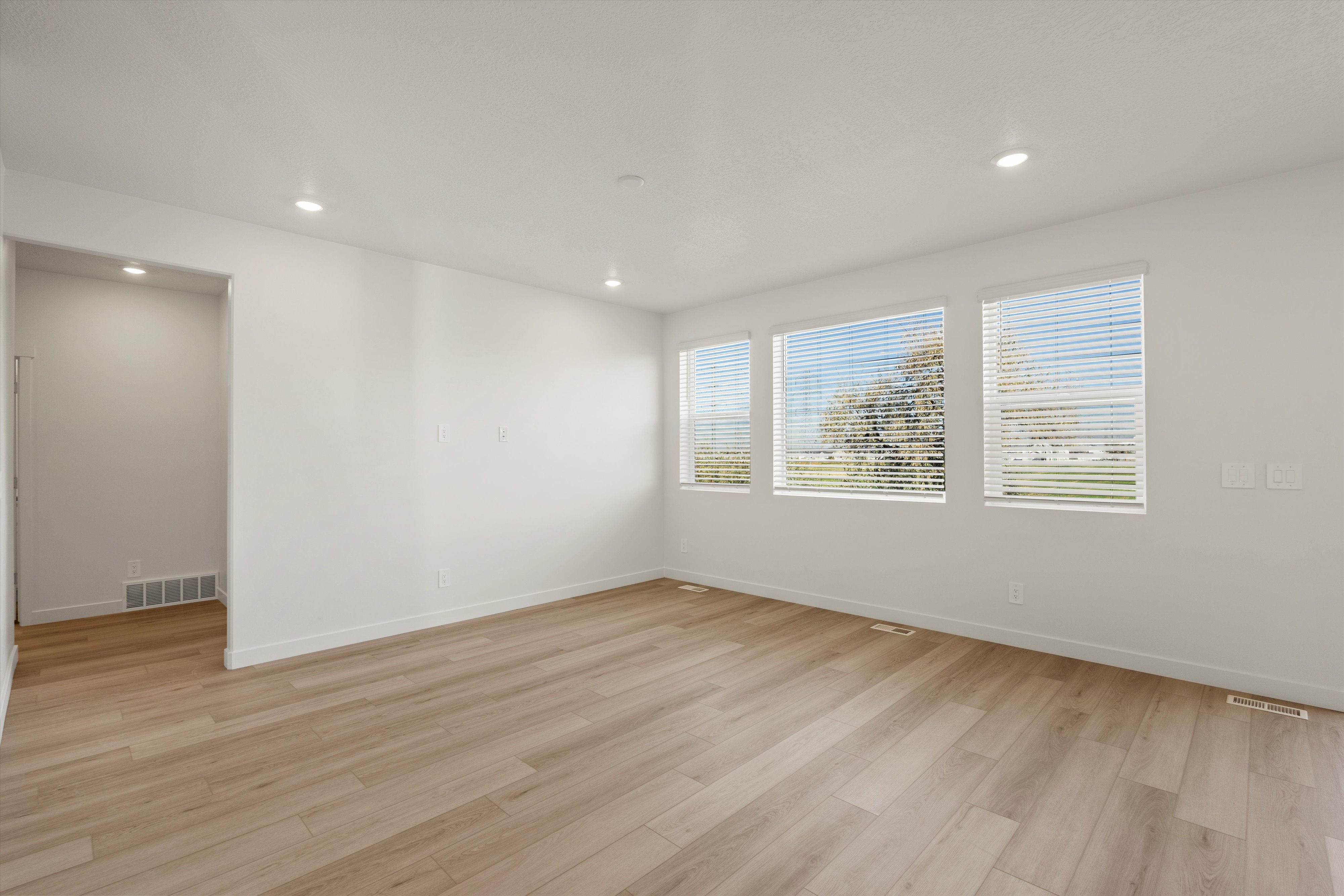 **DISCLAIMER** Interior package may vary. Open-concept living area featuring light wood-finish flooring, recessed lighting, and three large windows with white blinds