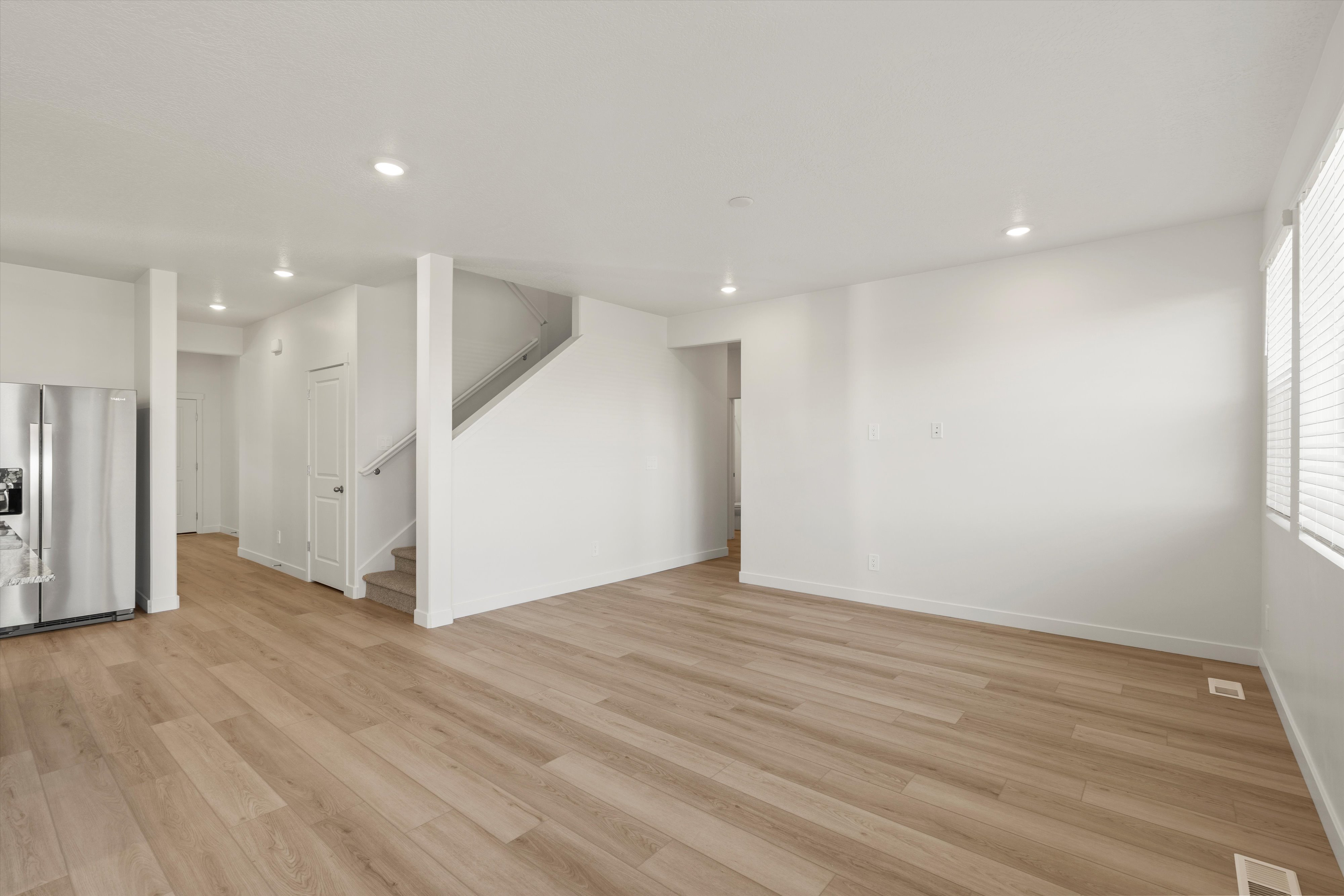 **DISCLAIMER** Interior package may vary. Open-concept living area featuring wood-finish flooring, recessed lighting, white walls, and a built-in stainless steel refrigerator