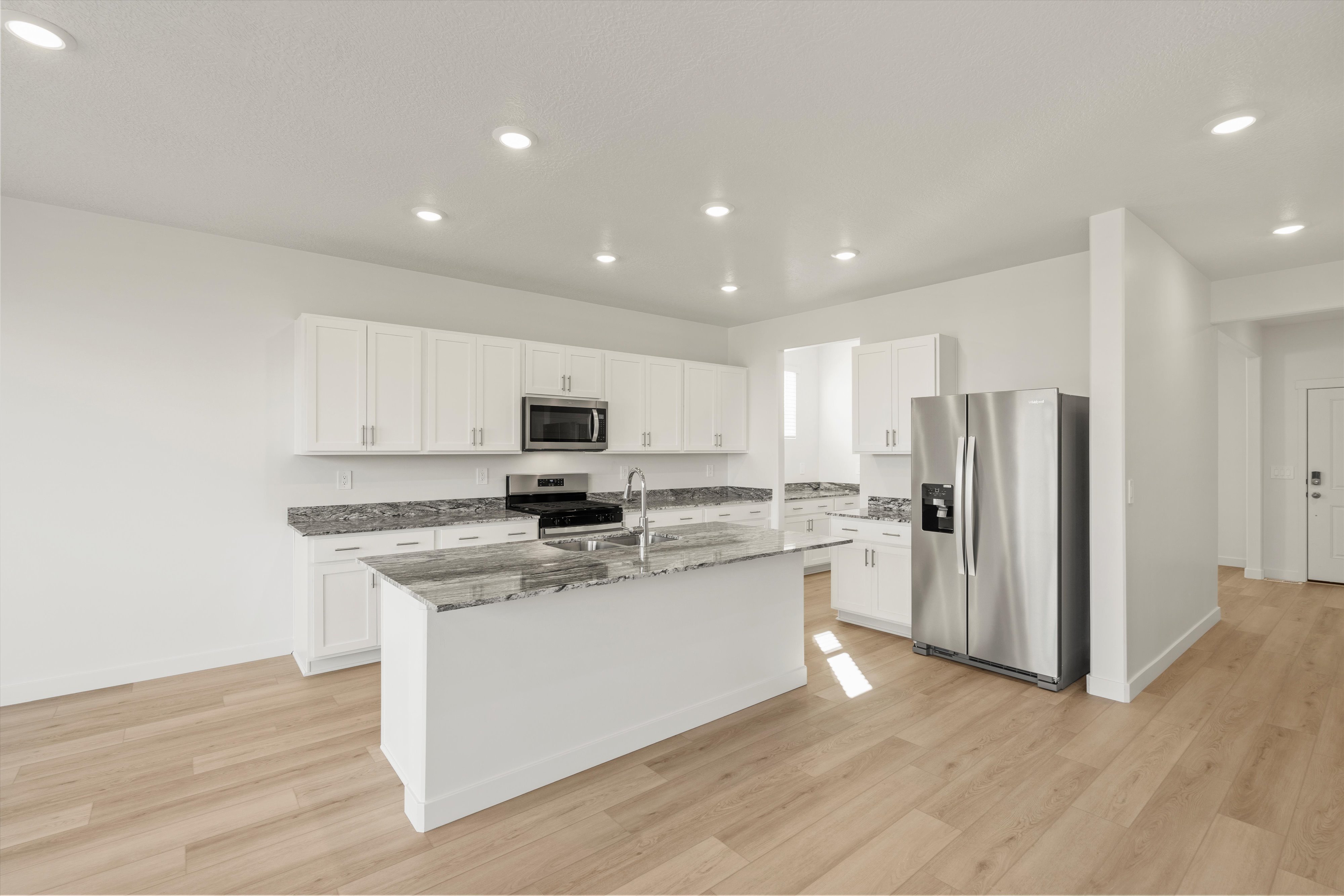 **DISCLAIMER** Interior package may vary. Open-concept kitchen featuring an island with a stainless steel sink, white cabinetry, speckled countertops, and wood-finish flooring