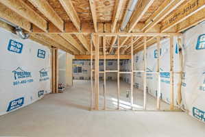Unfinished lower level featuring exposed wood joists and subfloor, concrete flooring, and framing for future customization