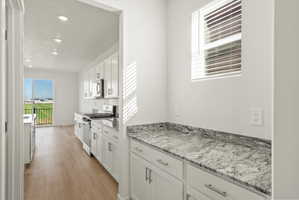 **DISCLAIMER** Interior package may vary. Kitchen featuring white shaker-style cabinetry, stainless steel appliances, speckled stone countertops, wood-finish flooring, and recessed lighting