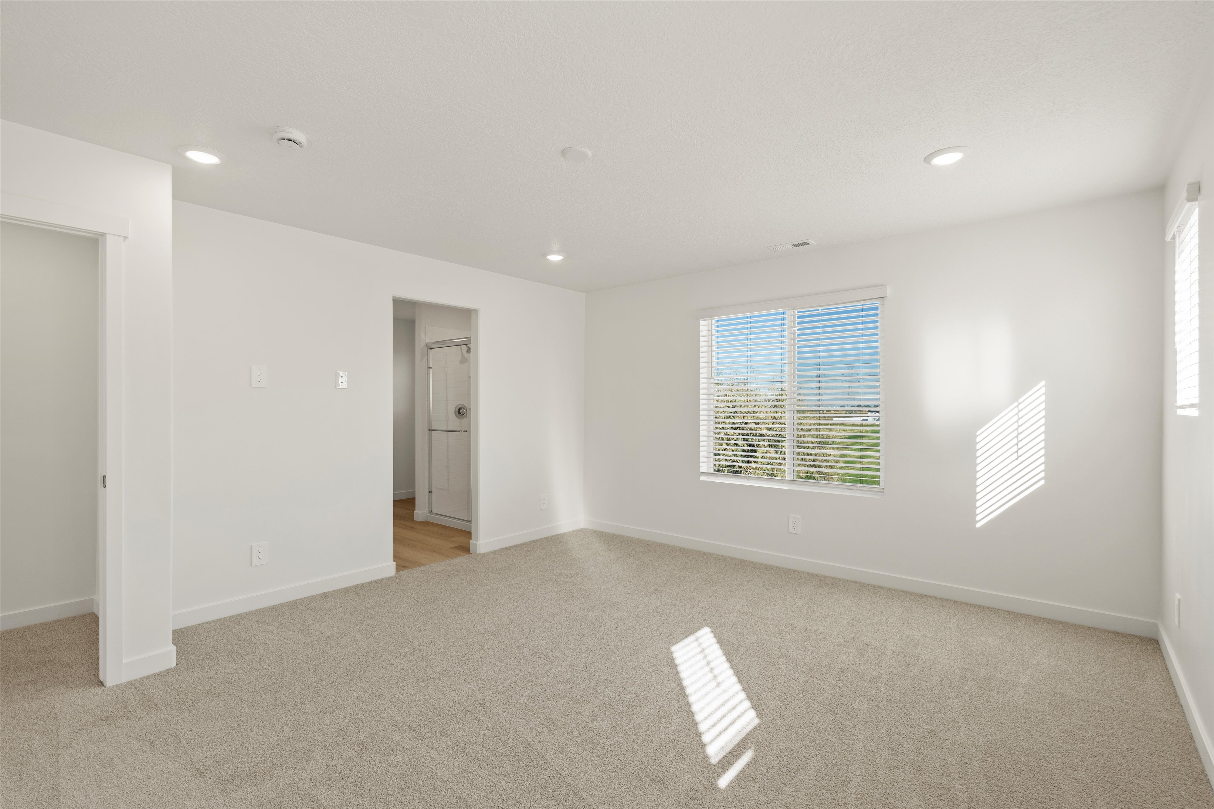 **DISCLAIMER** Interior package may vary. Carpeted room featuring a large window with horizontal blinds, recessed ceiling lighting, and crisp white walls