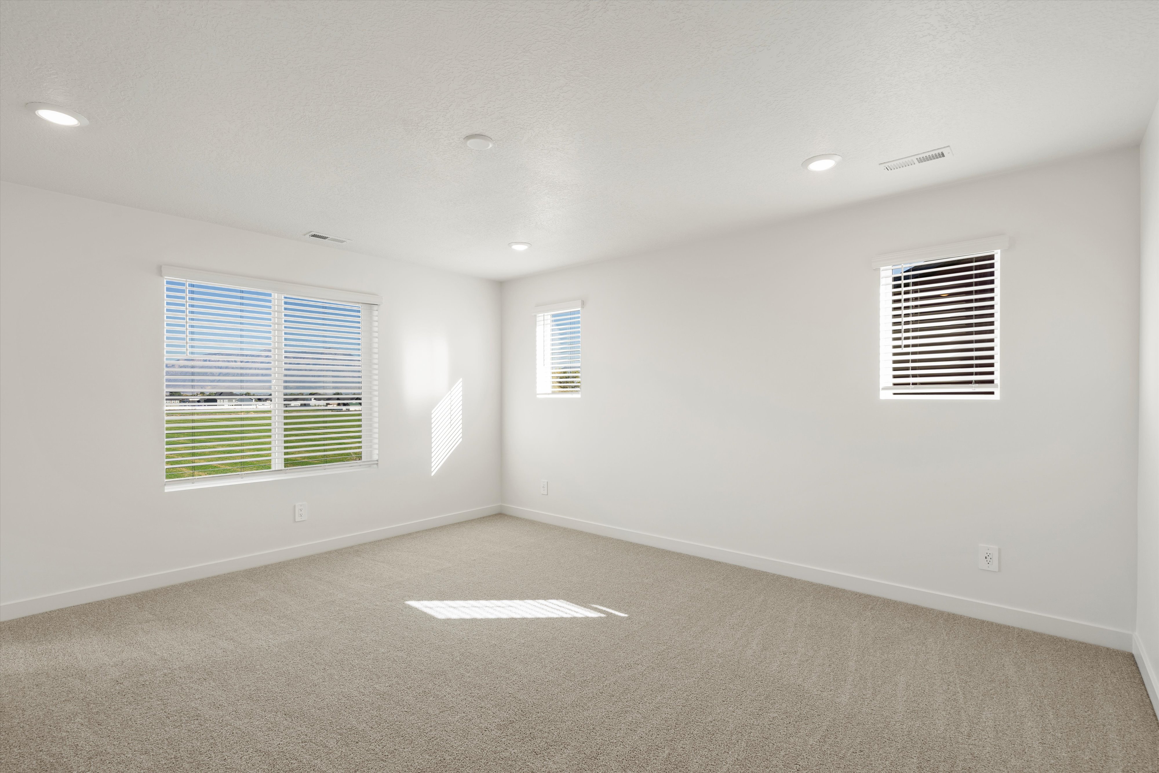 **DISCLAIMER** Interior package may vary. Bright room featuring a large window with horizontal blinds, neutral wall paint, recessed lighting, and soft carpet flooring