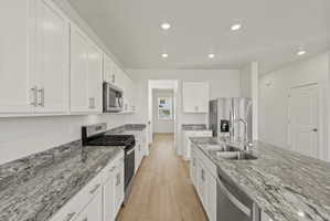 **DISCLAIMER** Interior package may vary. Kitchen featuring white shaker-style cabinetry, stainless steel appliances, speckled stone countertops, a double basin sink, and wood-finish flooring