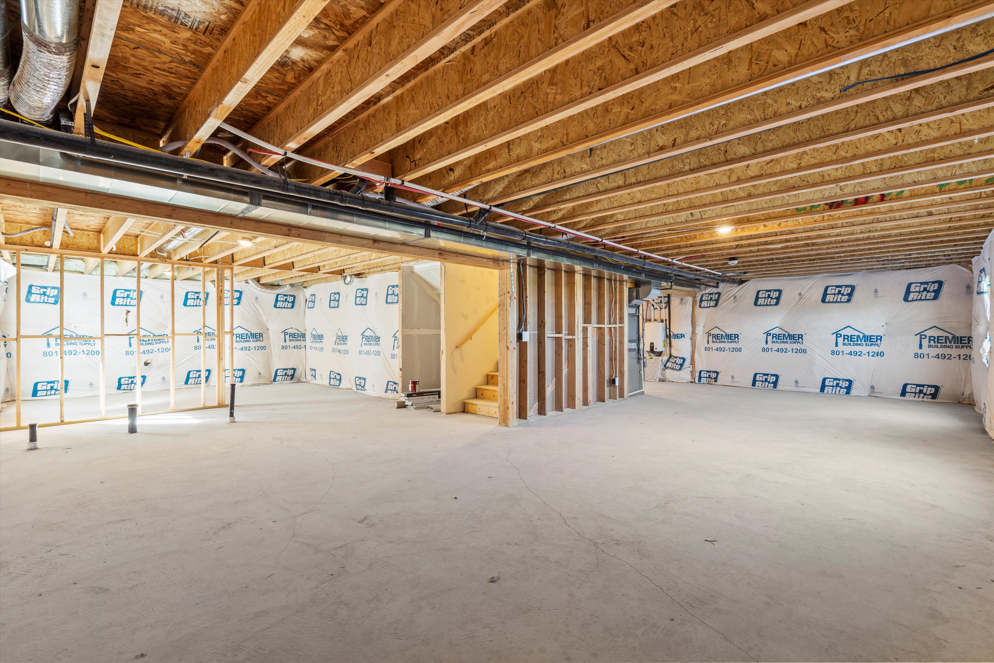Unfinished lower level featuring exposed wood joists and subfloor, partial framing, concrete flooring, and visible plumbing rough-ins