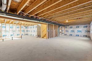Unfinished lower level featuring exposed wood joists and subfloor, partial framing, concrete flooring, and visible plumbing rough-ins