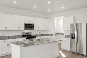 **DISCLAIMER** Interior package may vary. Modern kitchen featuring an island with an undermount sink, stainless steel appliances, white cabinetry, and granite countertops