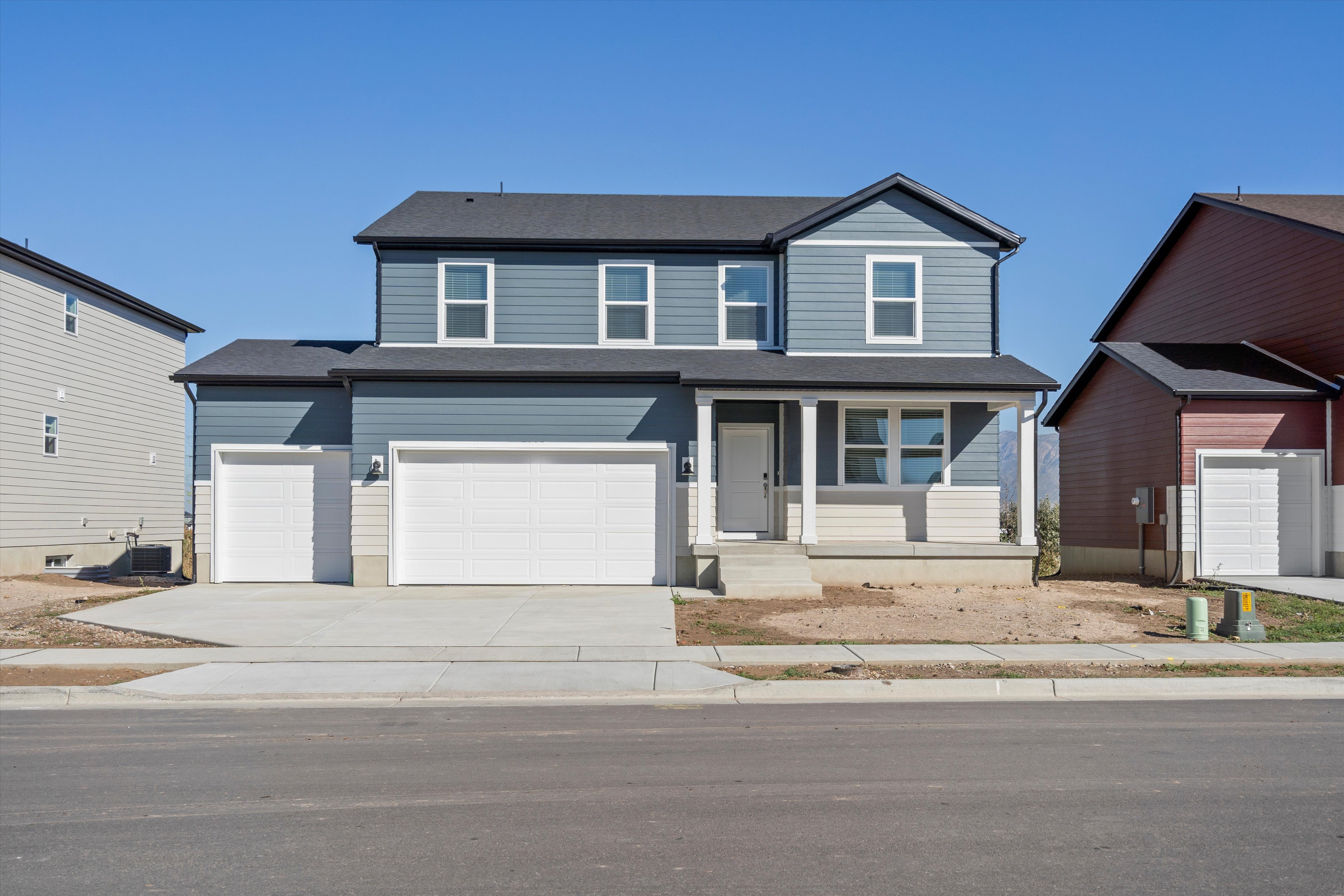 Contemporary two-story residence featuring a covered front porch, dark gray siding, light beige stone veneer accents, and a dual garage with white doors