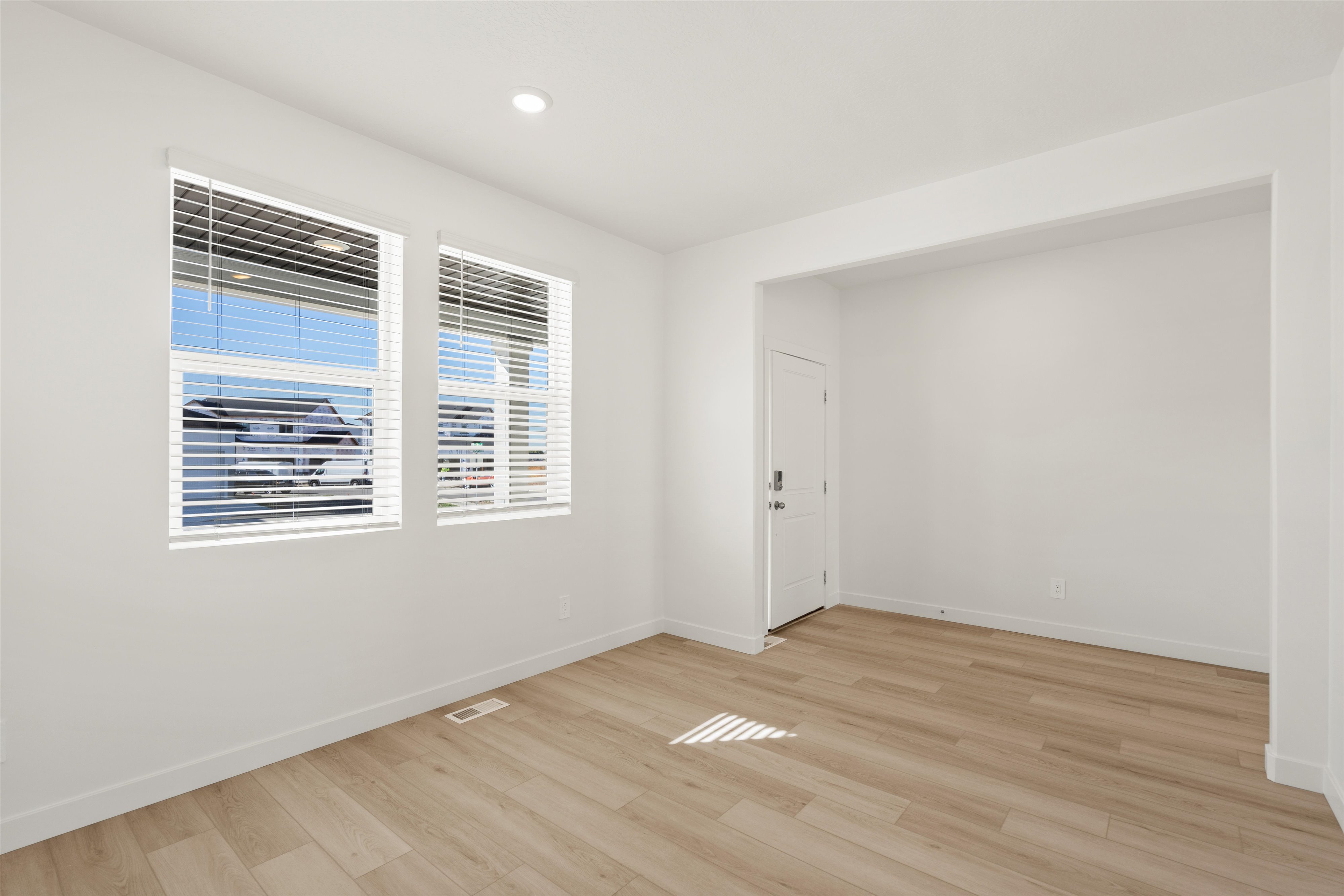 **DISCLAIMER** Interior package may vary. Bright interior space featuring two windows with horizontal blinds, wood-finish flooring, recessed lighting, and a white door with contemporary hardware