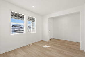 **DISCLAIMER** Interior package may vary. Bright interior space featuring two windows with horizontal blinds, wood-finish flooring, recessed lighting, and a white door with contemporary hardware